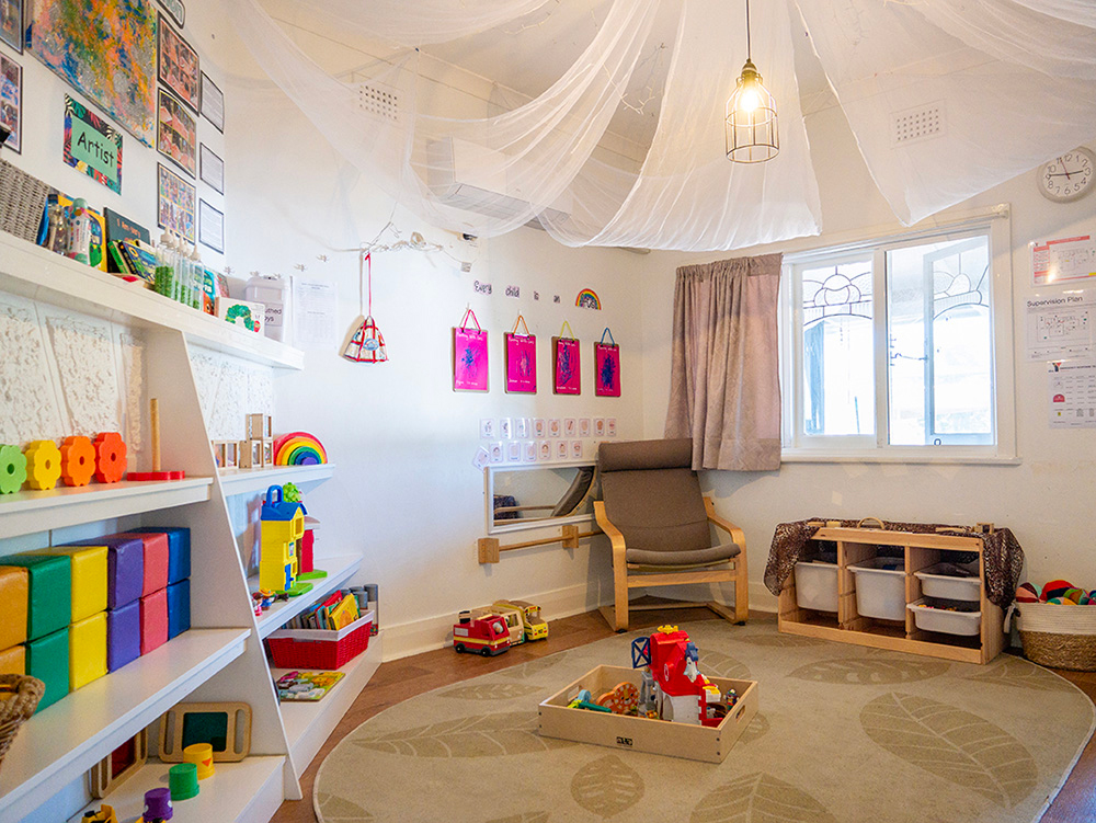 Nursery room with fabric canopy, colorful storage, reading nook, and natural light at Albany childcare centre