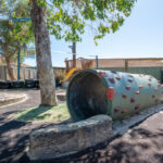 Large painted pipe climbing structure in outdoor play area at Albany childcare centre, with a tree and slide
