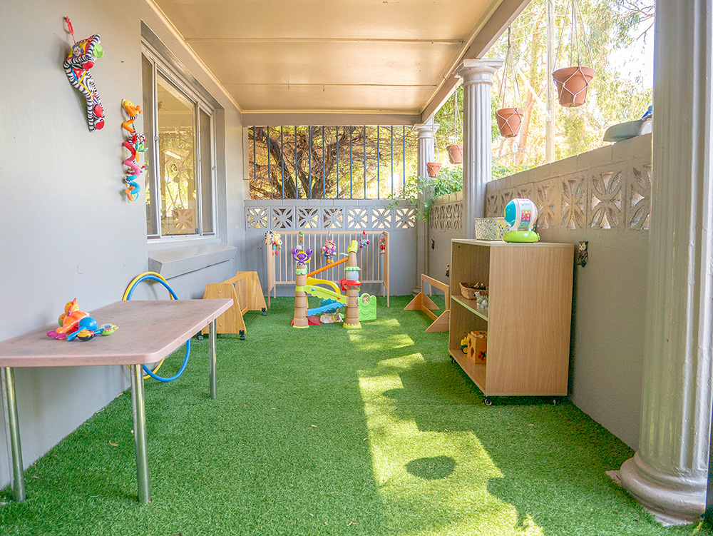 Covered outdoor play area with artificial turf and activity stations at East Cannington childcare