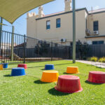 Shaded outdoor play area with colorful stepping blocks on artificial turf at Kalgoorlie centre
