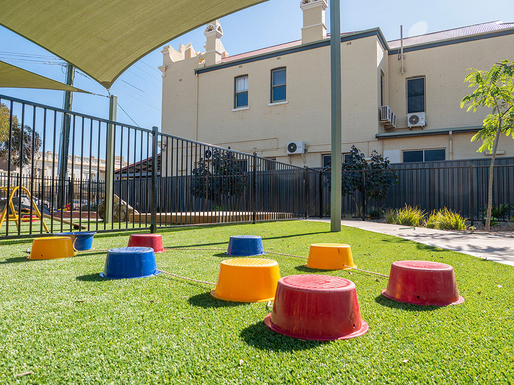 Shaded outdoor play area with colorful stepping blocks on artificial turf at Kalgoorlie centre