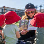 Educator reading outdoors with children in sun-safe hats at Kalgoorlie childcare centre