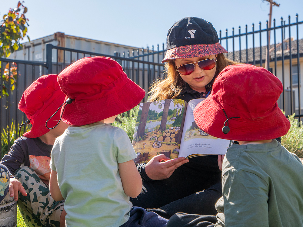 Educator reading outdoors with children in sun-safe hats at Kalgoorlie childcare centre