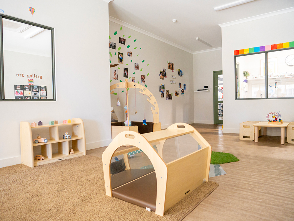 Infant play area with climbing equipment and family photos at Kalgoorlie childcare centre