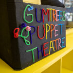 Handmade cardboard puppet theater with 'Gumtrees Puppet Theatre' in colorful pipe cleaner letters