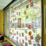 Large window decorated with Indigenous-inspired handprint art and designs overlooking outdoor play area at Gumtrees OSHC