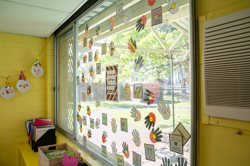 Large window decorated with Indigenous-inspired handprint art and designs overlooking outdoor play area at Gumtrees OSHC