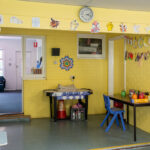 Bright yellow classroom at Gumtrees OSHC Service with children's artwork on walls, activity stations, and furniture