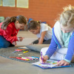 Children sitting on floor mats drawing and colouring during quiet creative time at Currambine OSHC School Holiday Program