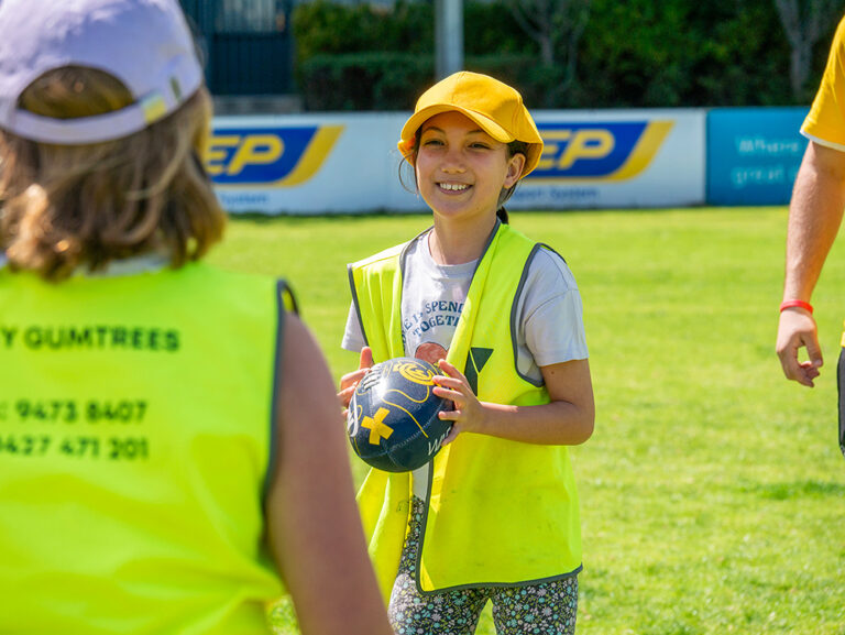 Smiling child holding football during Coles Healthy Kicks activity at Gumtrees School Holiday Program