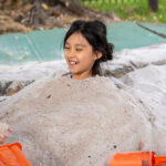 Smiling child buried in sand during outdoor play at Gumtrees OSHC School Holiday Program