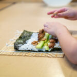 Child's hands rolling sushi with bamboo mat during cooking class at Gumtrees OSHC School Holiday Program