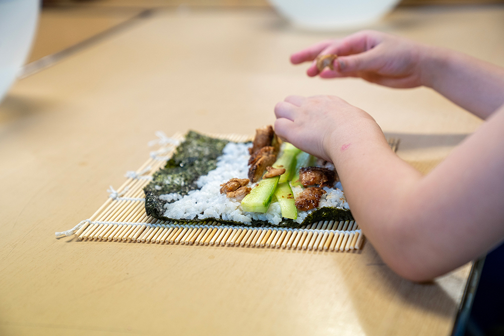 Child's hands rolling sushi with bamboo mat during cooking class at Gumtrees OSHC School Holiday Program