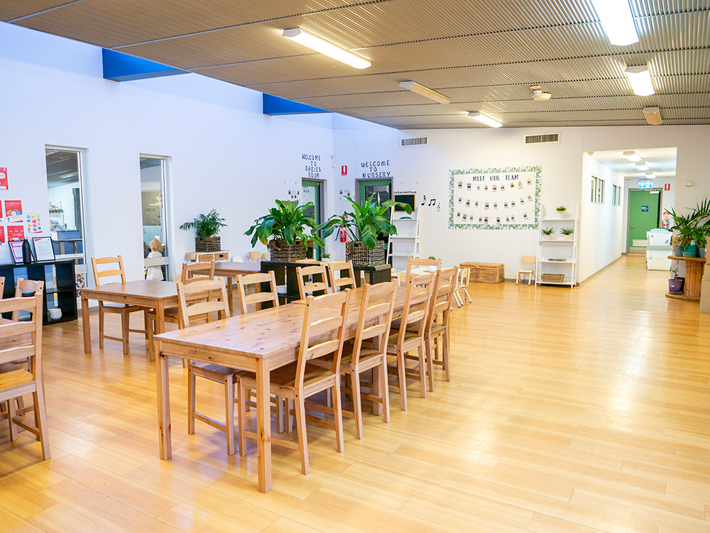Spacious dining area with timber tables and indoor plants at Port Hedland childcare centre