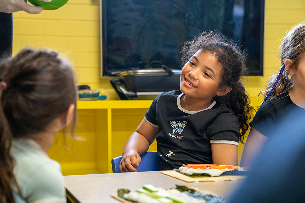 Smiling child making sushi with friends during cooking activity at Gumtrees OSHC School Holiday Program