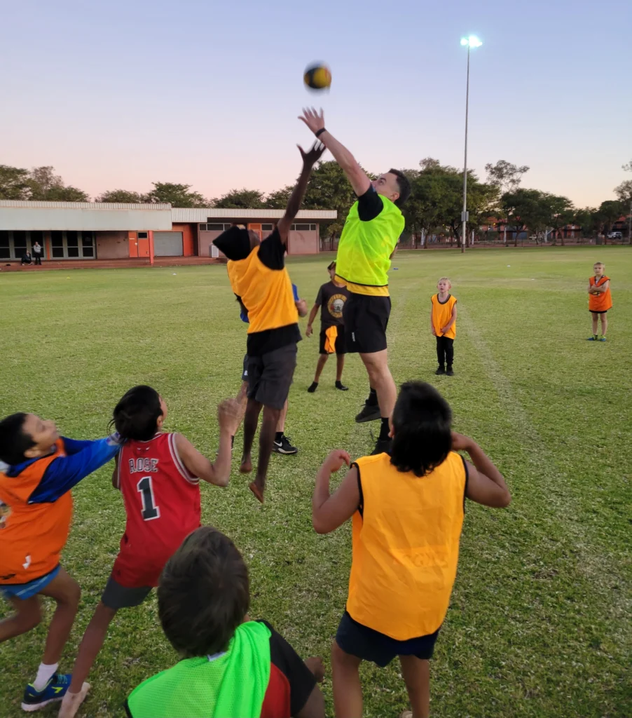 group of children in neon bibs playing basketball outside on an oval