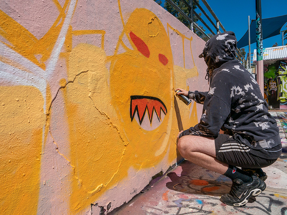 Street artist crouched down painting street art mural with spray paint