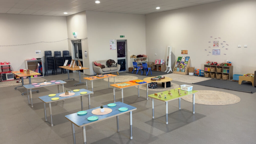 A bright, open children's care room set up with activity tables laid with colourful plates and learning materials, surrounded by play areas and bookshelves