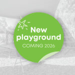 A promotional graphic announcing a new playground coming in 2026, overlaid on a greyscale photo of an existing children's play area