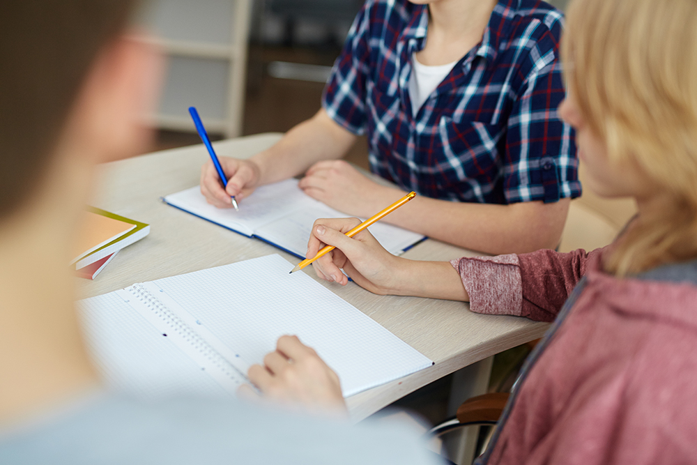 Close up image of group of young people writing in a notebook