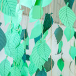 Strings of hand-cut paper leaves in various shades of green hanging as a decorative display in an early learning centre room