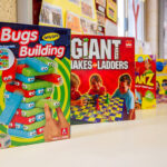 Boxed board games including Bugs Building and Giant Snakes and Ladders displayed on OSHC shelf