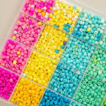 A plastic organiser tray filled with pink, yellow, and teal pony beads sorted by colour