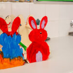 Two hand-painted wooden Easter bunny shapes in red and blue sitting on a bench near a sink