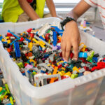 A child's hand reaches into a large bin overflowing with colourful LEGO bricks