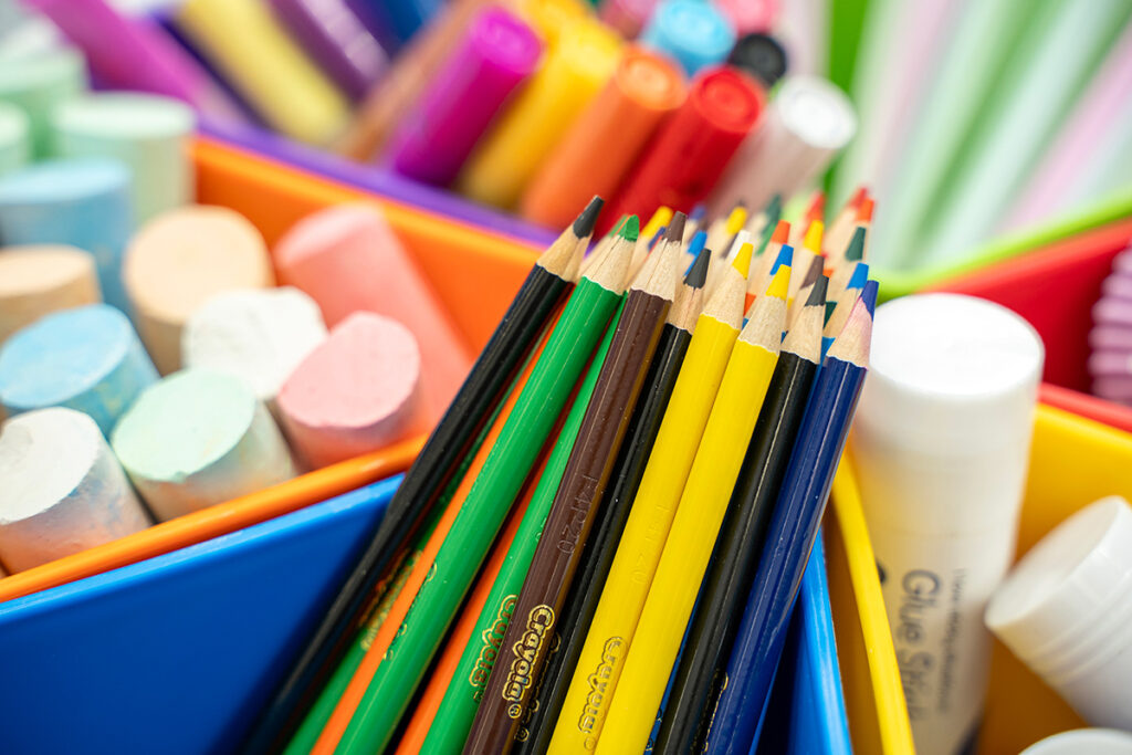 Close-up of Crayola coloured pencils, erasers, and glue sticks sorted into colourful plastic trays