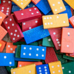 A pile of colourful wooden dominoes in red, blue, yellow, orange, and green scattered together