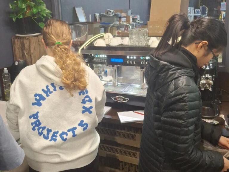 Two young people using a coffee machine to make coffee as part of a barista course