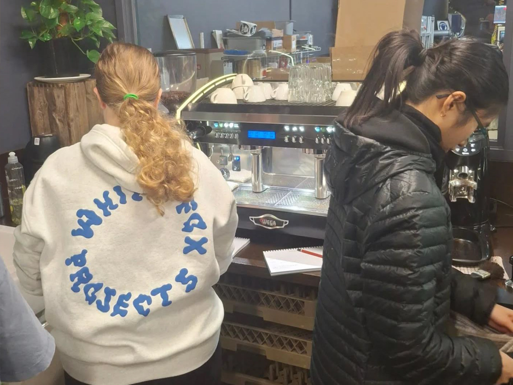 Two young people using a coffee machine to make coffee as part of a barista course