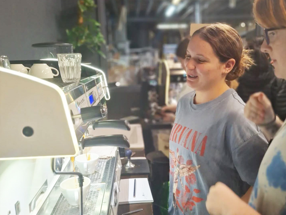 Two young people standing at a coffee machine and watching as they make coffee
