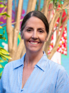 Smiling Y WA Board Member Jacinda in a blue and white striped top, photographed outdoors against a colourful mural backdrop