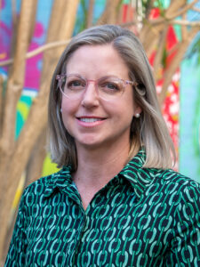Smiling Y WA Board Member Penelope in a green and black top, photographed outdoors against a colourful mural backdrop
