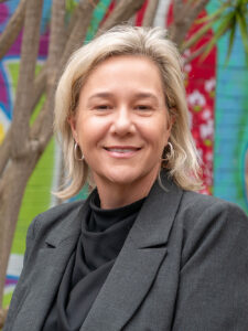 Smiling Y WA Board Member Samantha in a Black blazer and top, photographed outdoors against a colourful mural backdrop