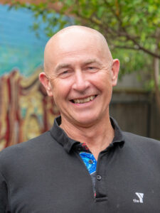 Smiling Y WA executive David in a black Y polo shirt, photographed outdoors against a colourful mural backdrop.