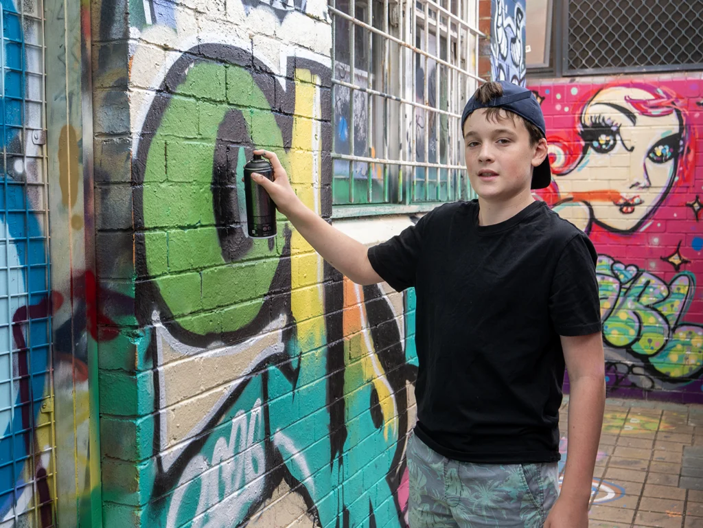 Young boy with cap doing street art on a wall