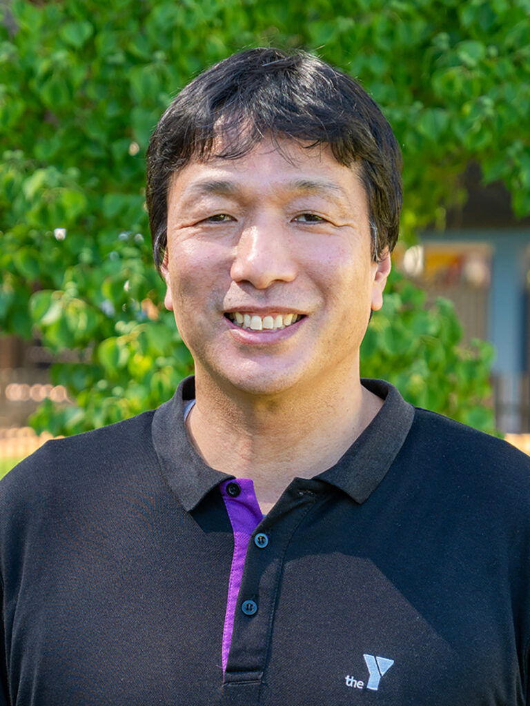 Professional headshot of smiling OSHC supervisor in purple Indigenous-design shirt outdoors