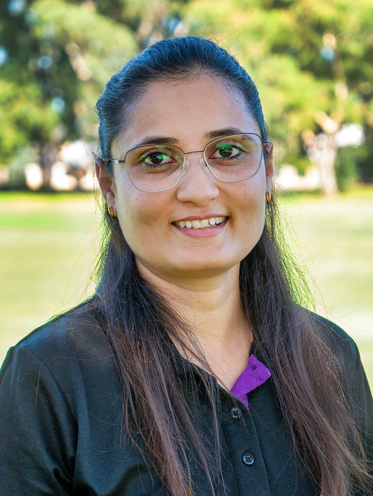 Smiling OSHC educator in YMCA uniform with name badge standing in outdoor garden setting