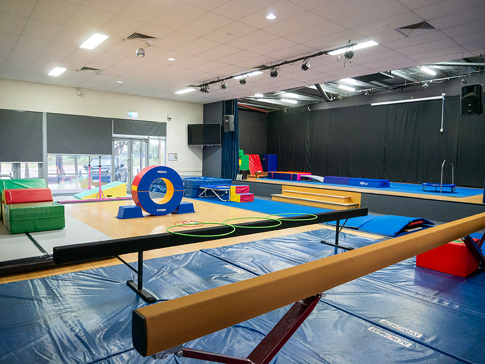 A gymnastics studio set up with a balance beam, foam shapes, hoops, and a colourful tunnel on a sprung wooden floor