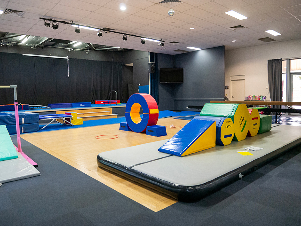 A gymnastics studio with colourful foam equipment, an air track mat, and a bar set up for a children's class
