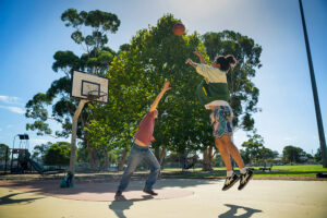 Two young people playing basketball on an outside basketball court