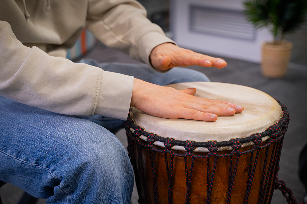 Close-up of a young person's hands playing a djembe drum during an indoor drumming session