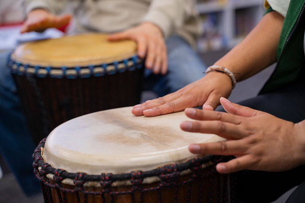 Close-up of two young people's hands playing djembe drums together during a group drumming activity