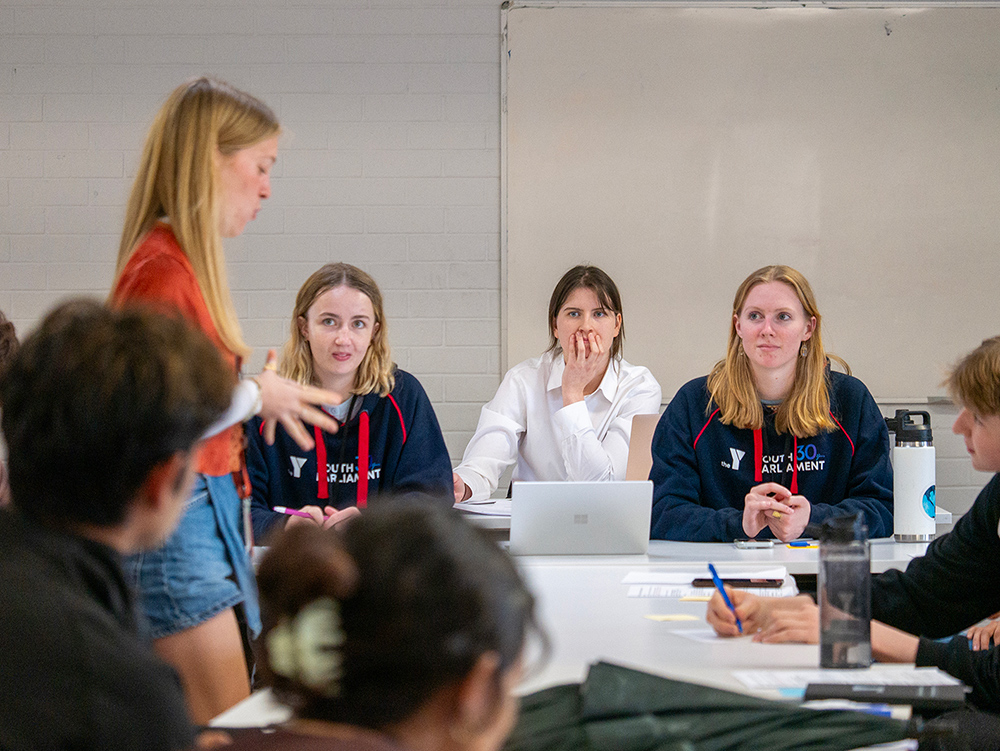 Young participants in the Y WA Youth Parliament hoodies listening attentively during a training session as a fellow participant speaks