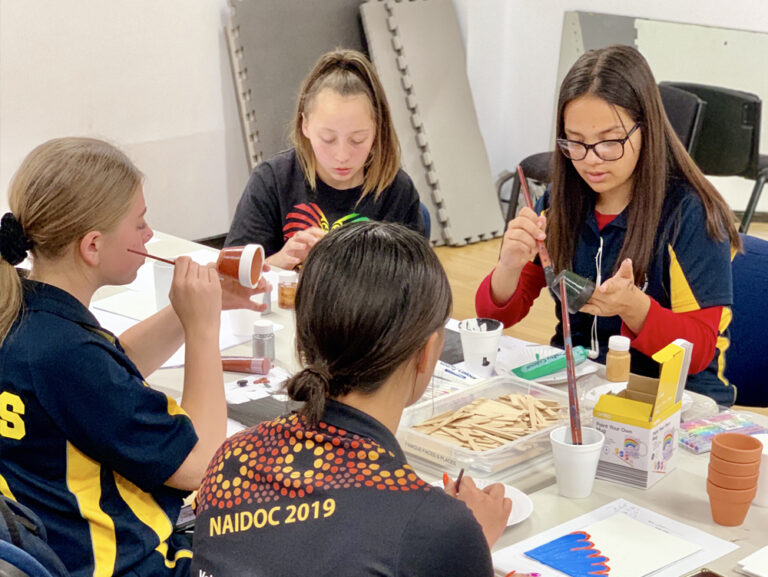 Group of young girls painting pot plants and doing other crafts at a table