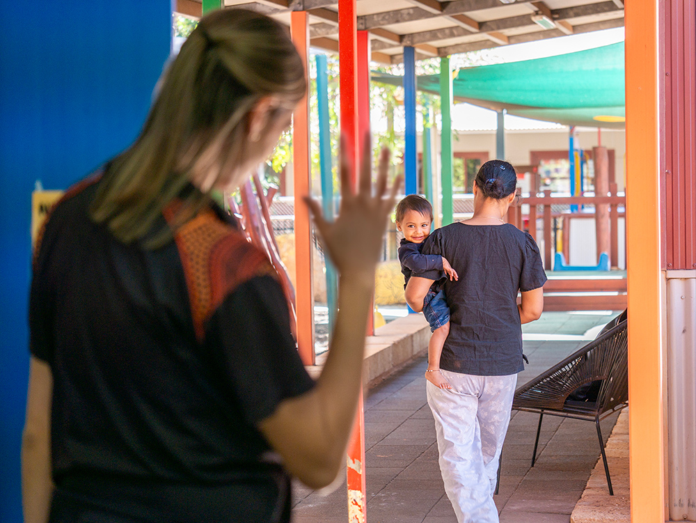 Staff member waving to child during childcare pick-up at colorful early learning Centre entrance