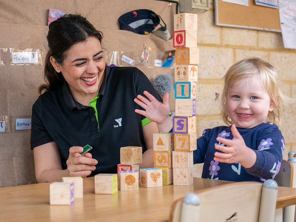 Early learning educator and toddler celebrating successful wooden block tower construction together